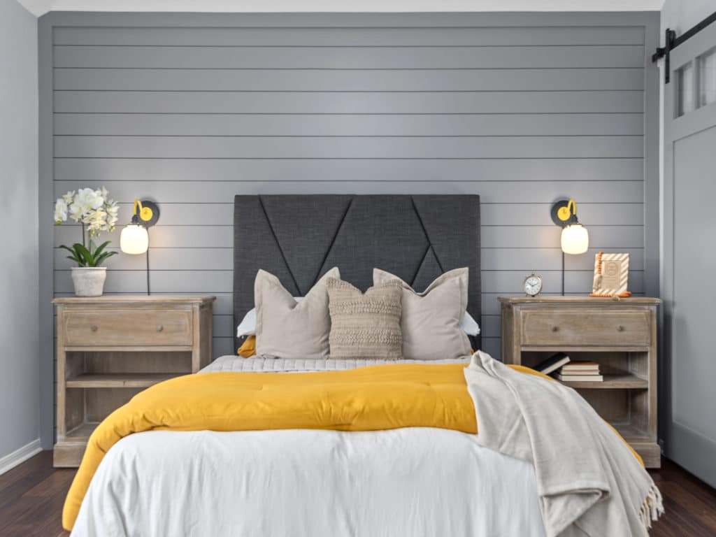 Small, well staged bedroom with bed and yellow throw blanket.